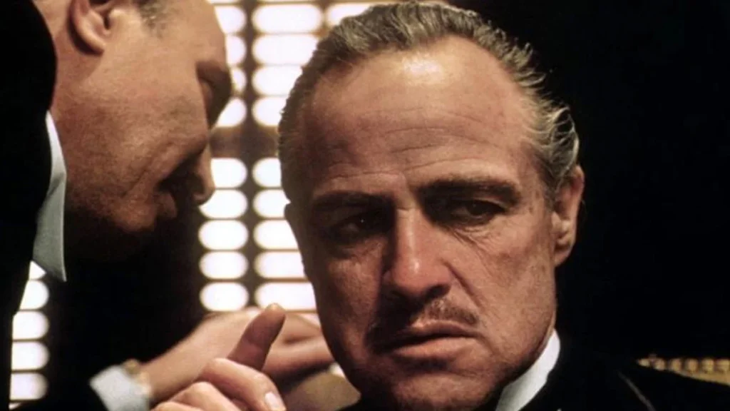 Don Vito Corleone e um homem falando ao seu ouvido