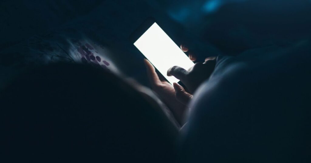 Homem olhando o celular no escuro